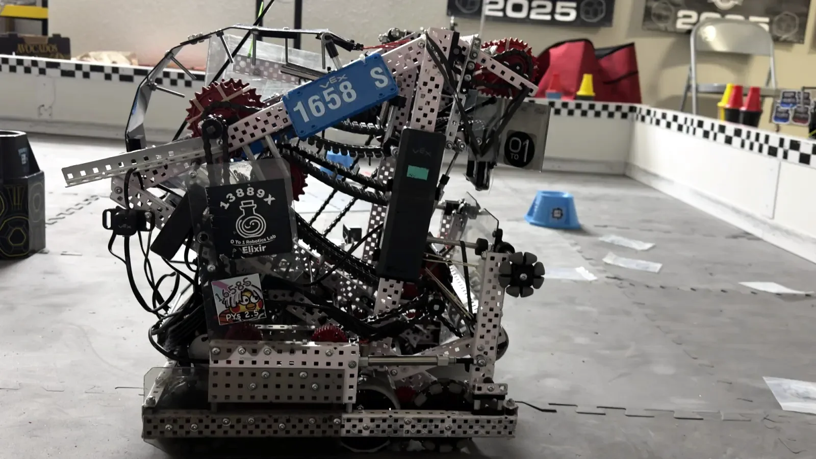 Team 1658S’s Push Back robot on a practice field, its blue 1658S plate on the side, with a 2025 banner on the wall behind