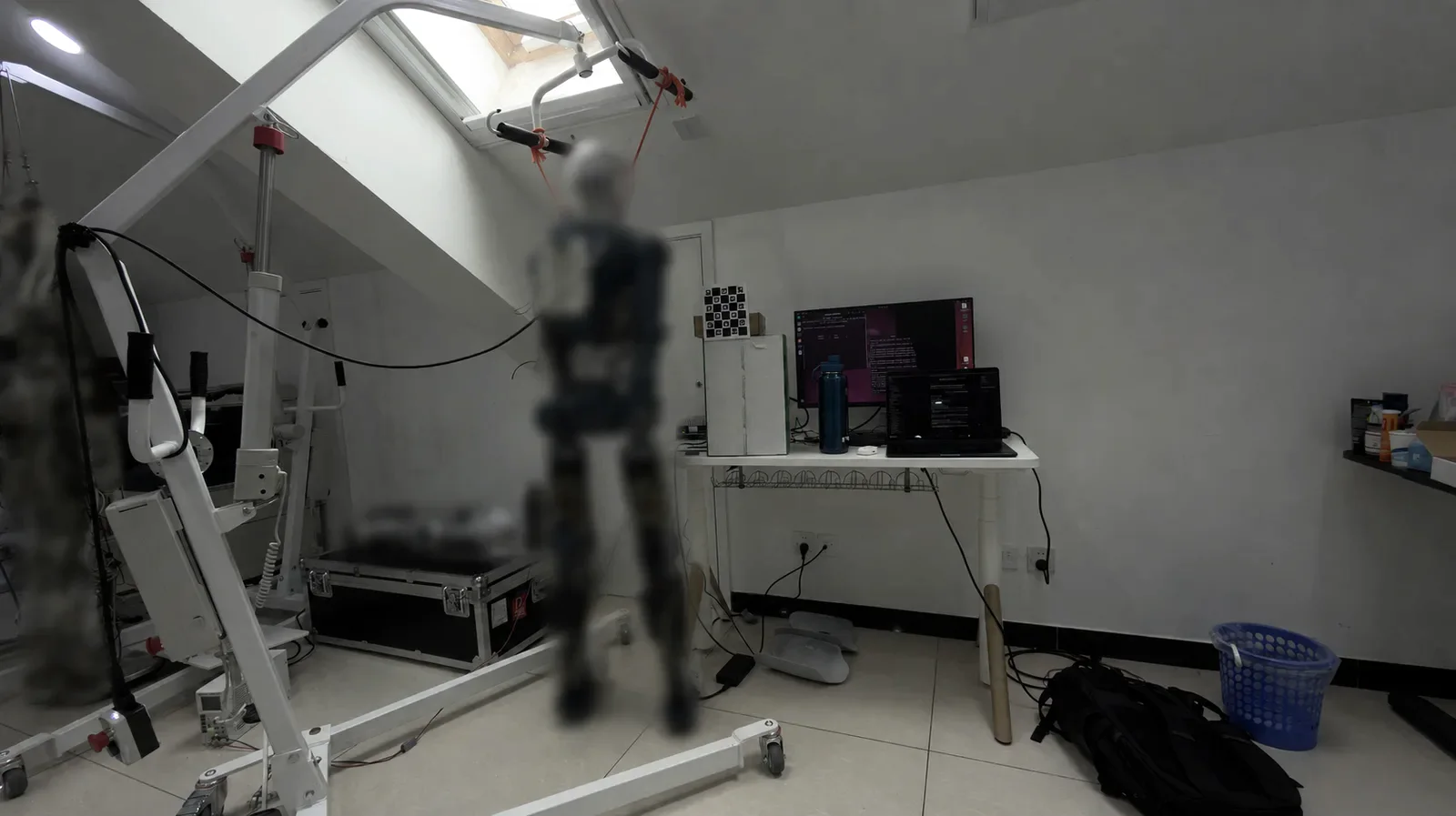 The humanoid robot hanging from shoulder ropes on a rolling frame in the test room, beside the calibration computer